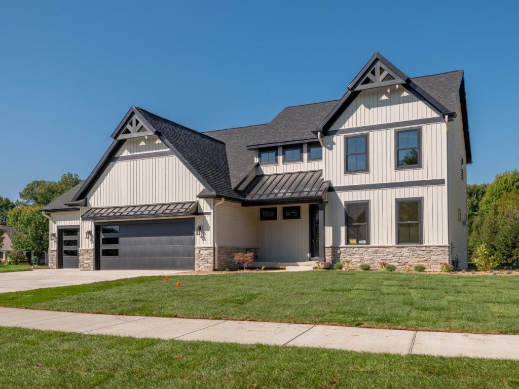 A modern two-story house with gray siding and black accents, featuring a three-car garage and a freshly landscaped lawn under a clear blue sky.