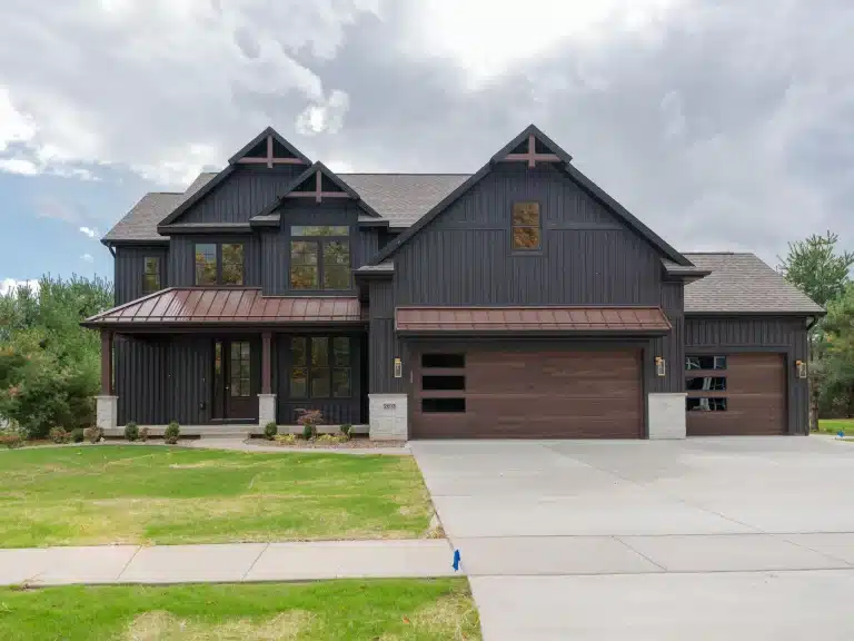 Two-story modern farmhouse with dark vertical siding, a large three-car garage, a wide driveway, and a covered front porch.