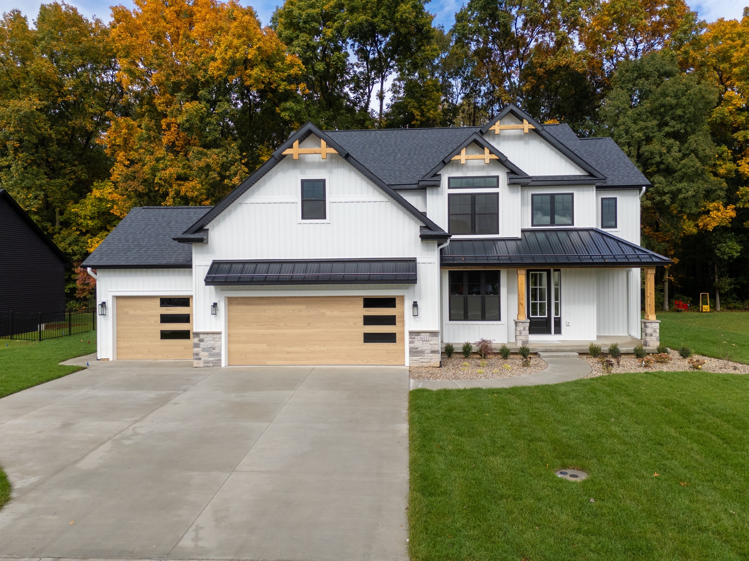 Front of the white modern farmhouse at 2612 Ashford Trail with black trim, cedar gable accents and a wood-look three-car garage.