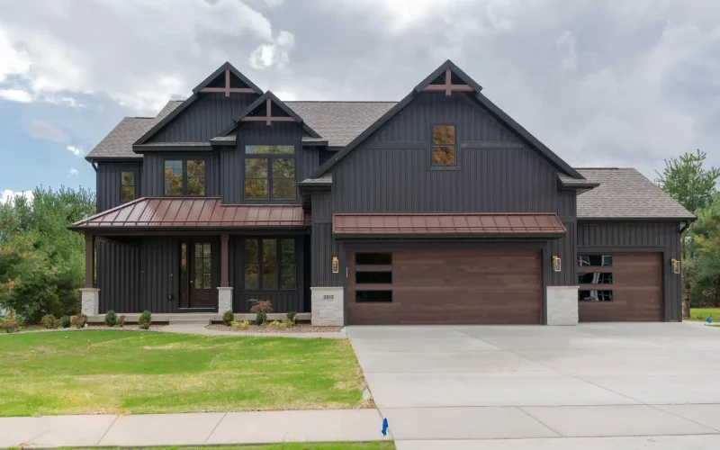 Two-story modern farmhouse with dark vertical siding, a large three-car garage, a wide driveway, and a covered front porch.