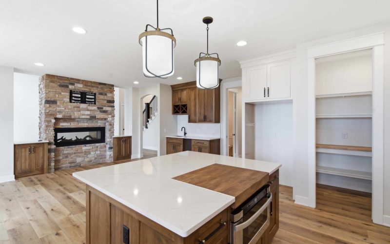 Modern kitchen with wood floors, island with dual surfaces, built-in shelves, white cabinets, stone fireplace, and pendant lights.